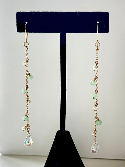 A pair of long dangly earrings with pearls and jade displayed on a black stand, against a white background.