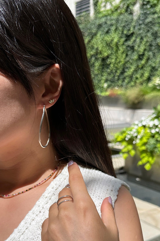 A person wearing large wavy hoop earrings made of sterling silver.