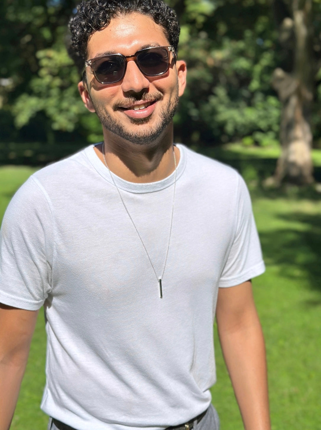 Man wearing sunglasses and a white t-shirt in a park setting