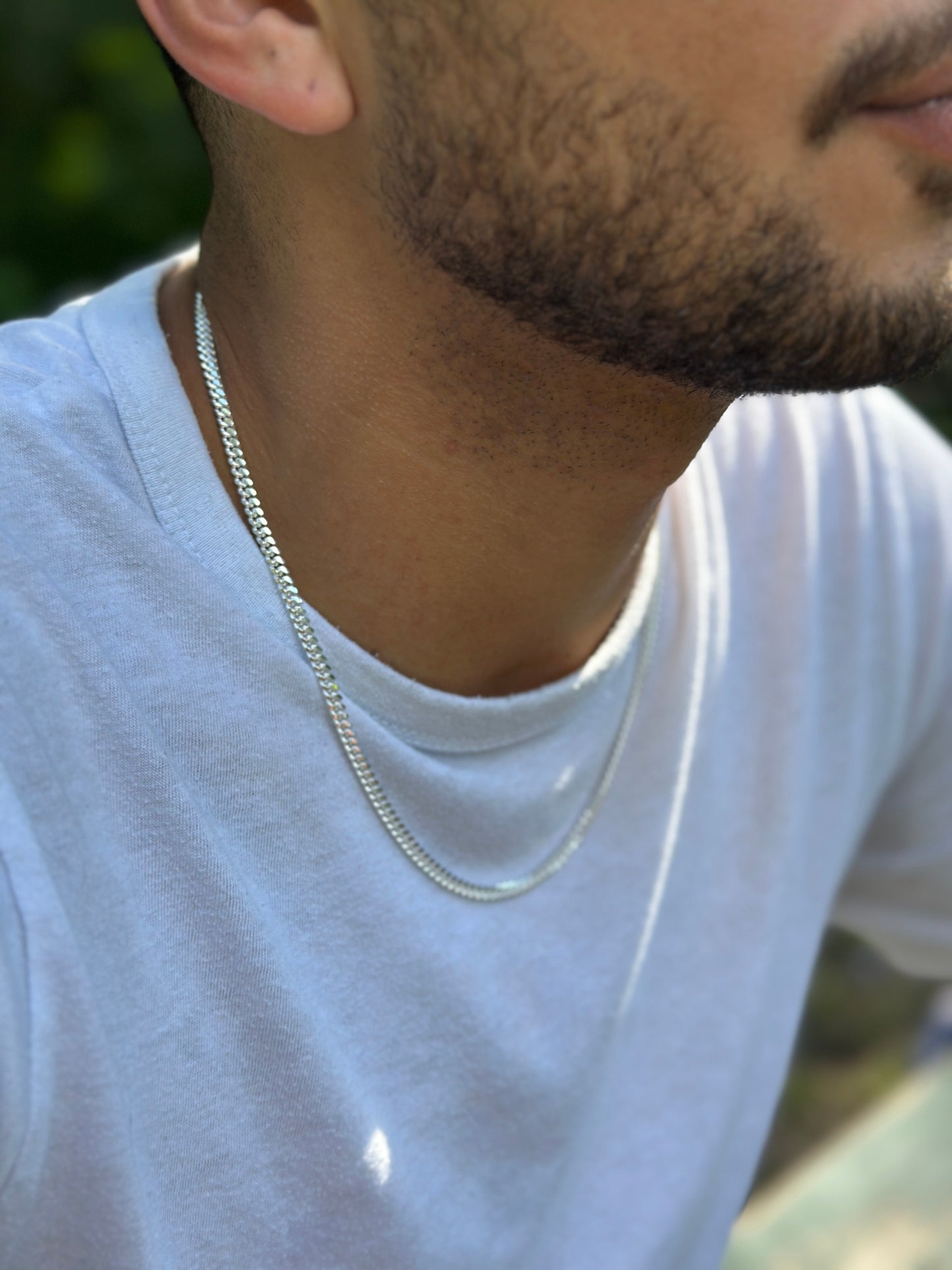 Close-up of a person wearing a silver chain necklace with a blurred natural background