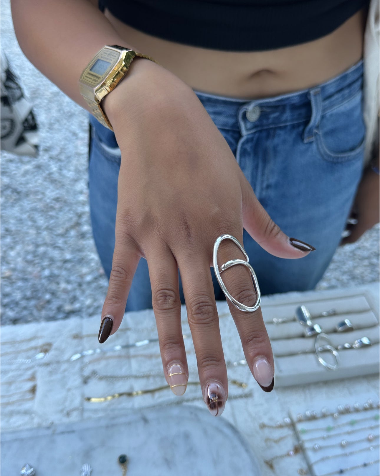 Hand with gold ring and black nail polish wearing a gold watch, with a blurred background.