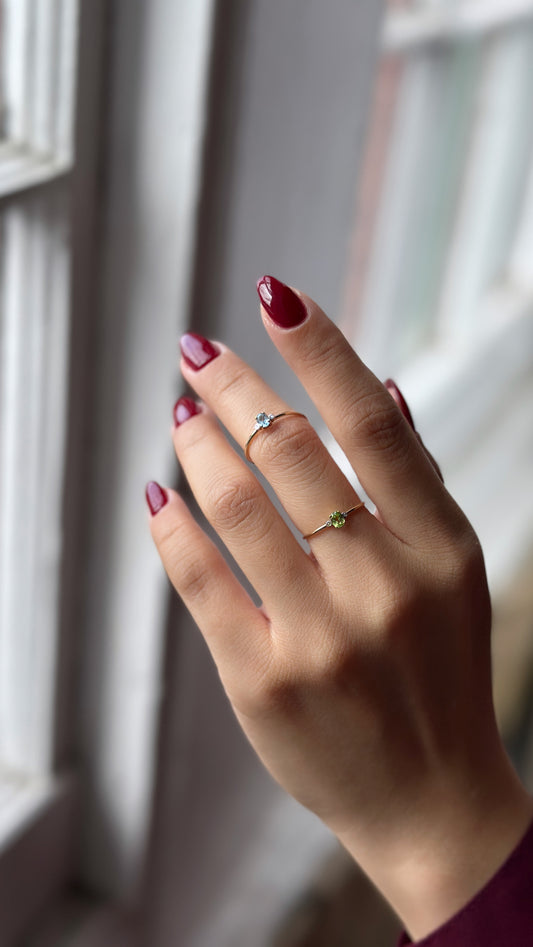 A person's hand displaying two gemstone rings in solid gold.