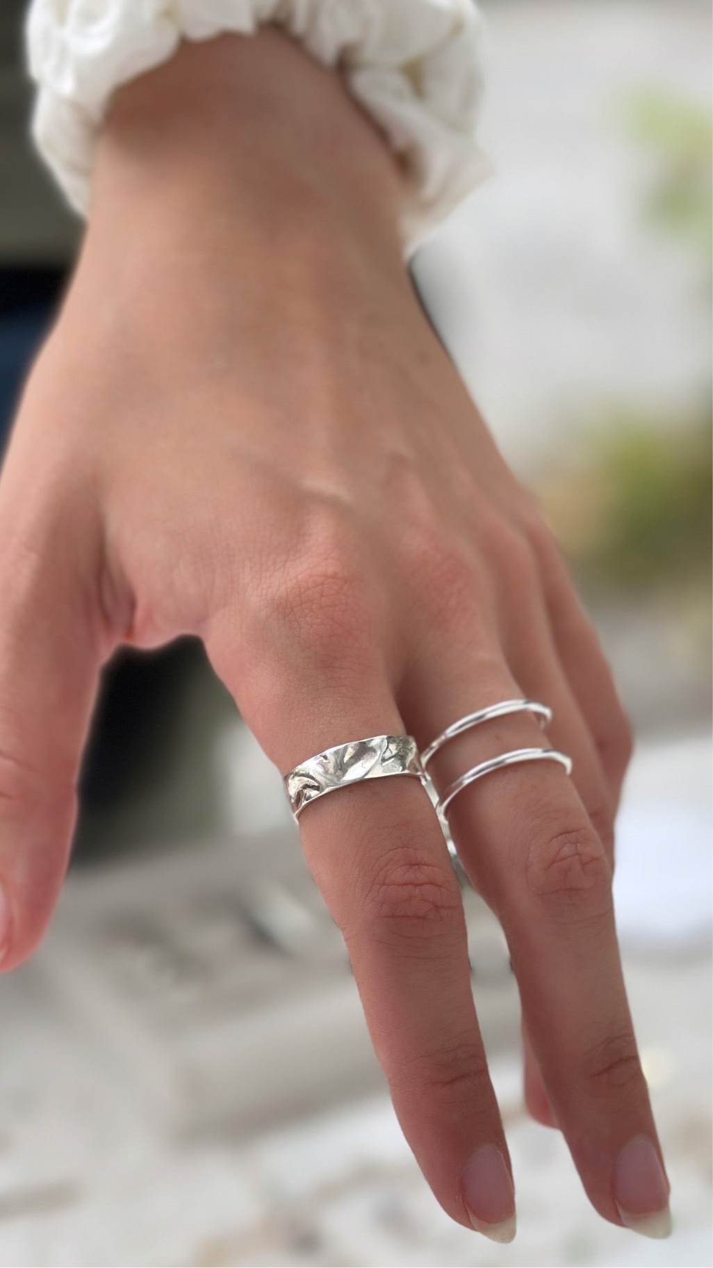 Close-up of a hand wearing multiple silver rings on a blurred background