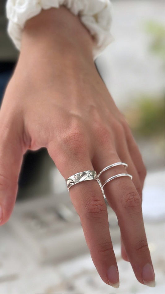 Close-up of a hand wearing multiple silver rings on a blurred background