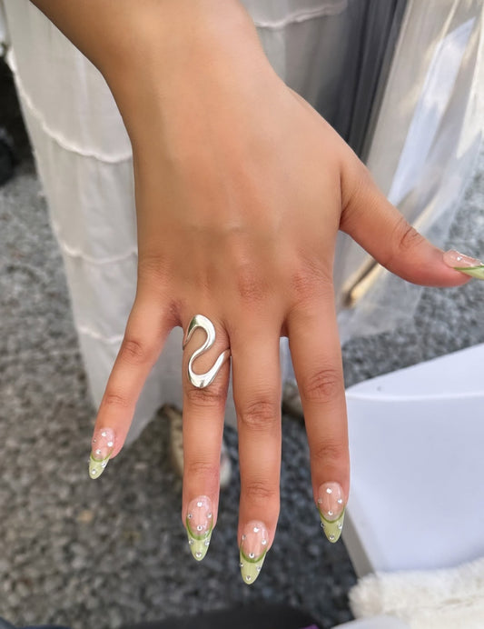 A person's hand displaying a sterling silver ring with a wavy design on a finger, with a blurred background.