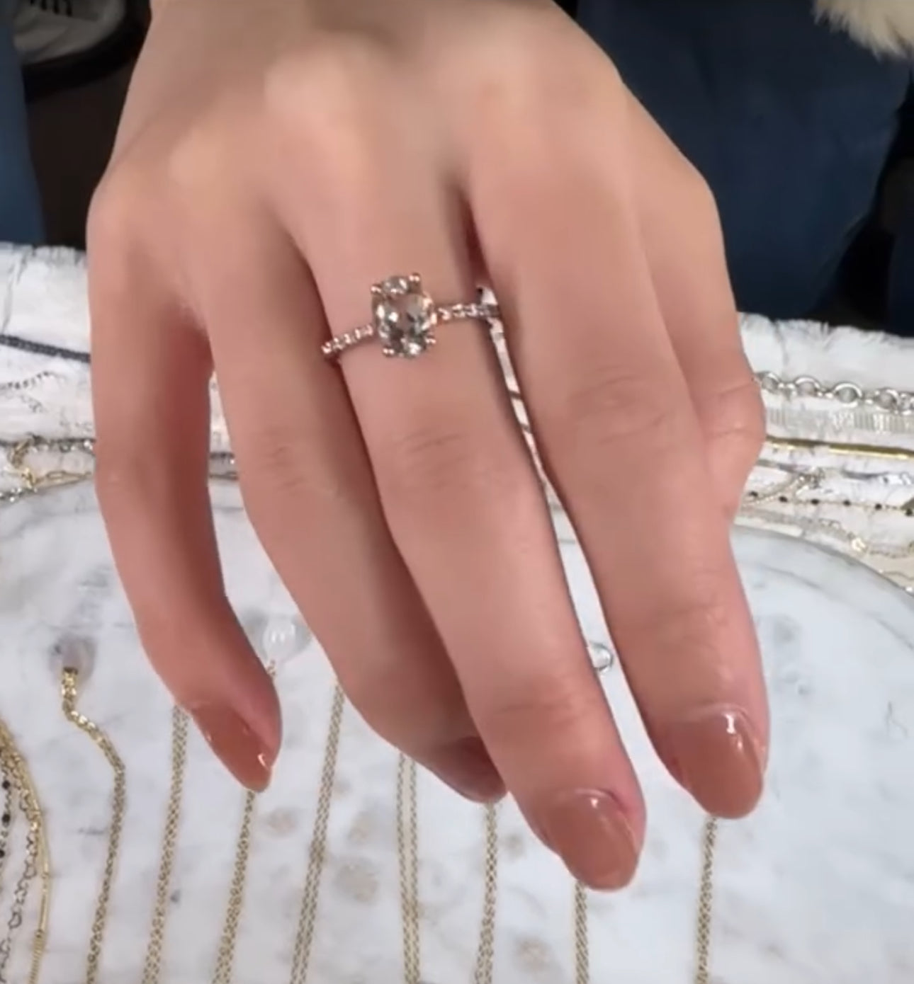 Close-up of a hand wearing a silver ring on a textured surface with jewelry.