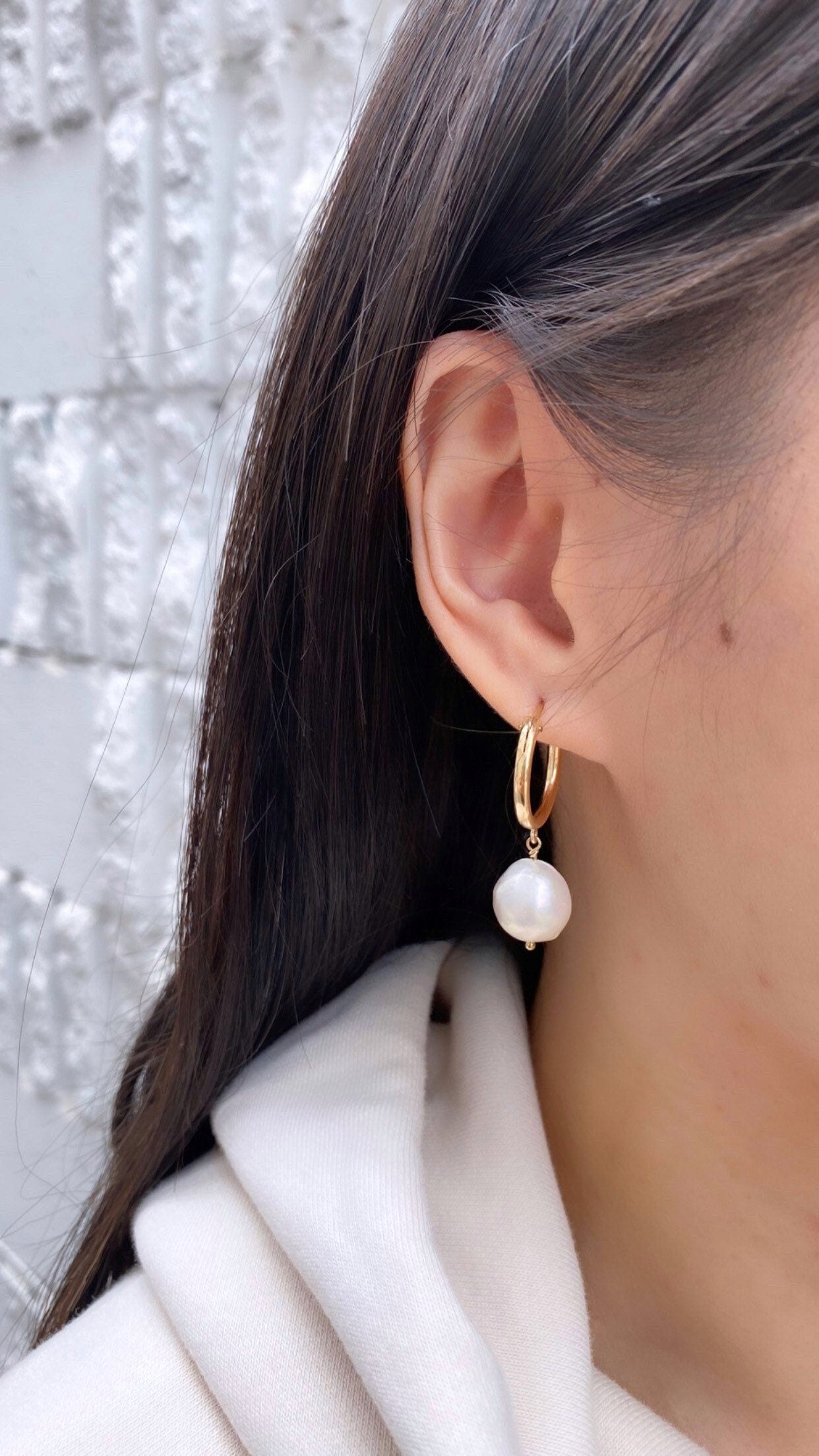 model wearing gold filled baroque pearl hoop earrings against brick wall