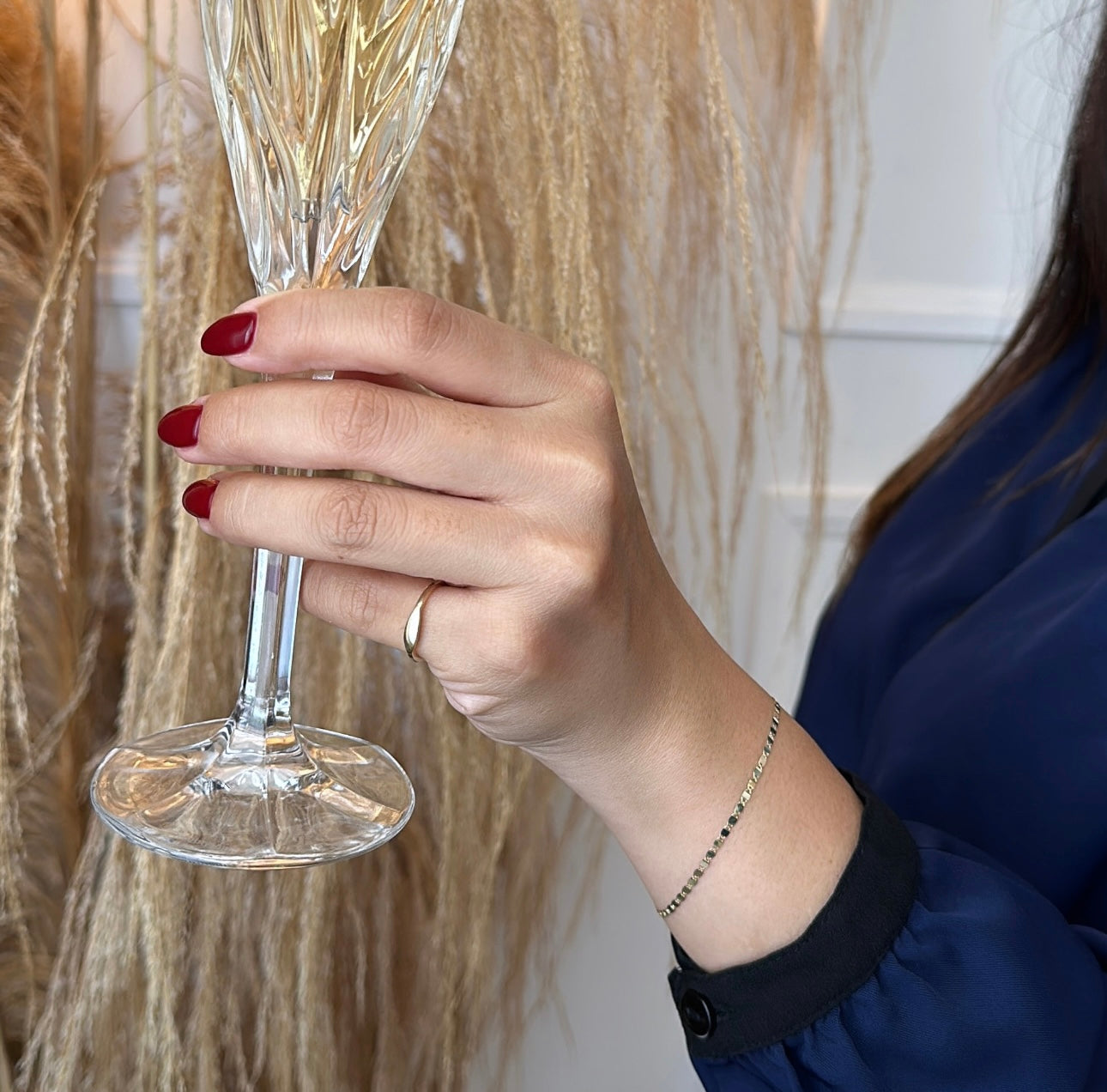 A person holding a glass of champagne, with the dainty signet ring on their finger.