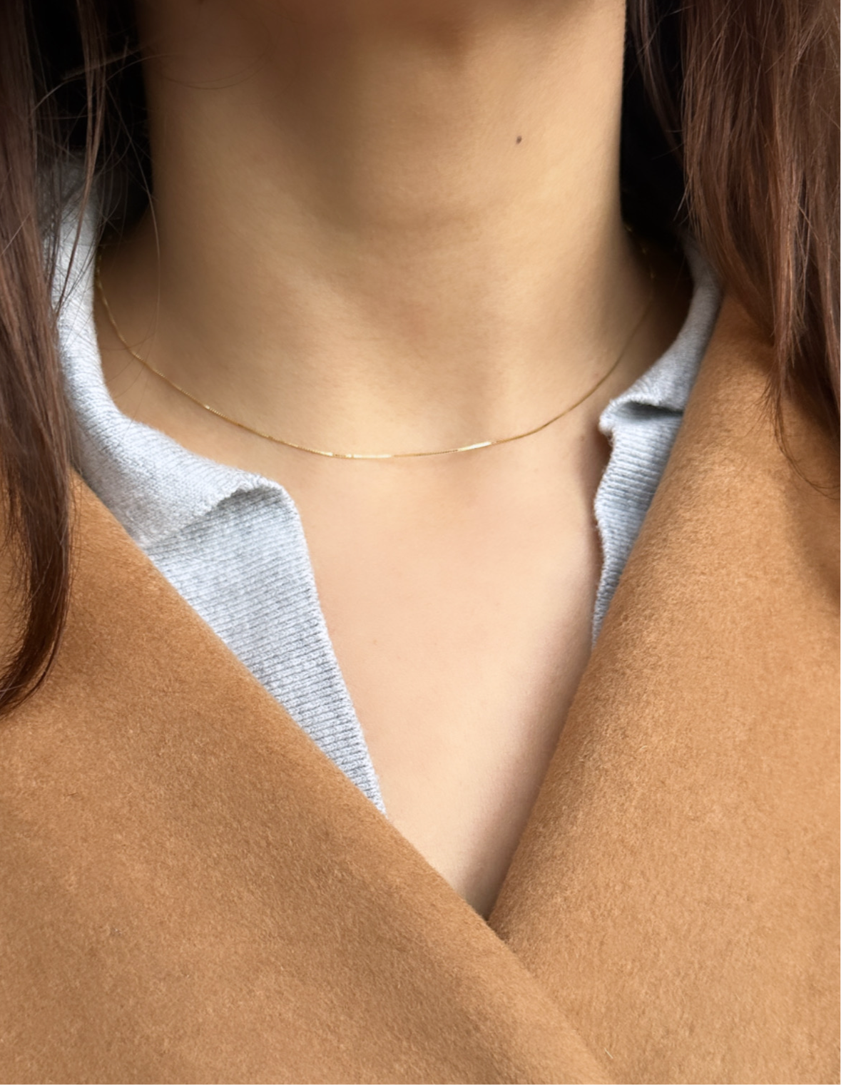 A close-up image of a person wearing a gold paperthin box chain necklace made of 10K solid gold.