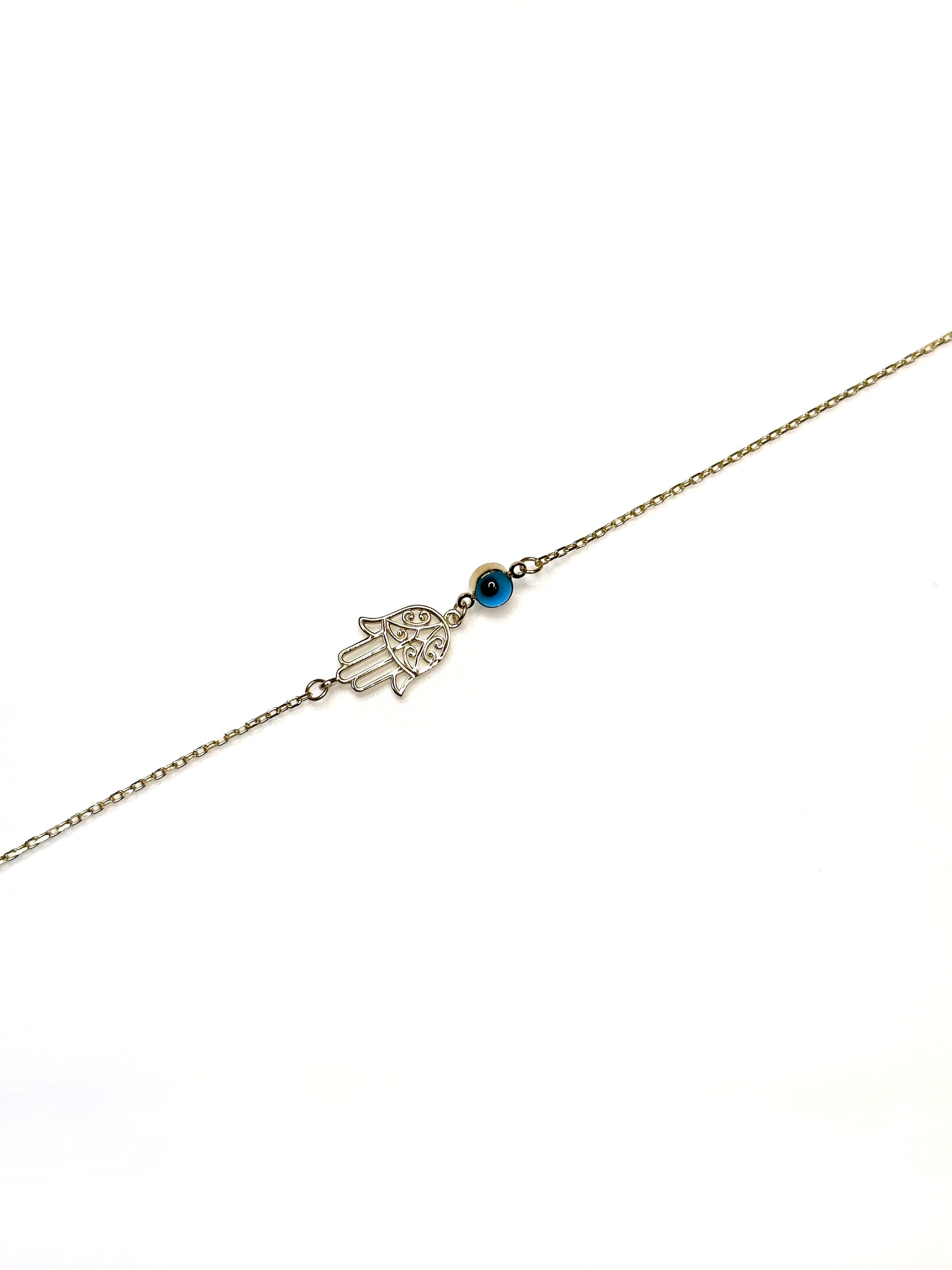 A gold bracelet featuring a Hamsa hand charm and a vibrant cobalt blue evil eye charm on a white background.