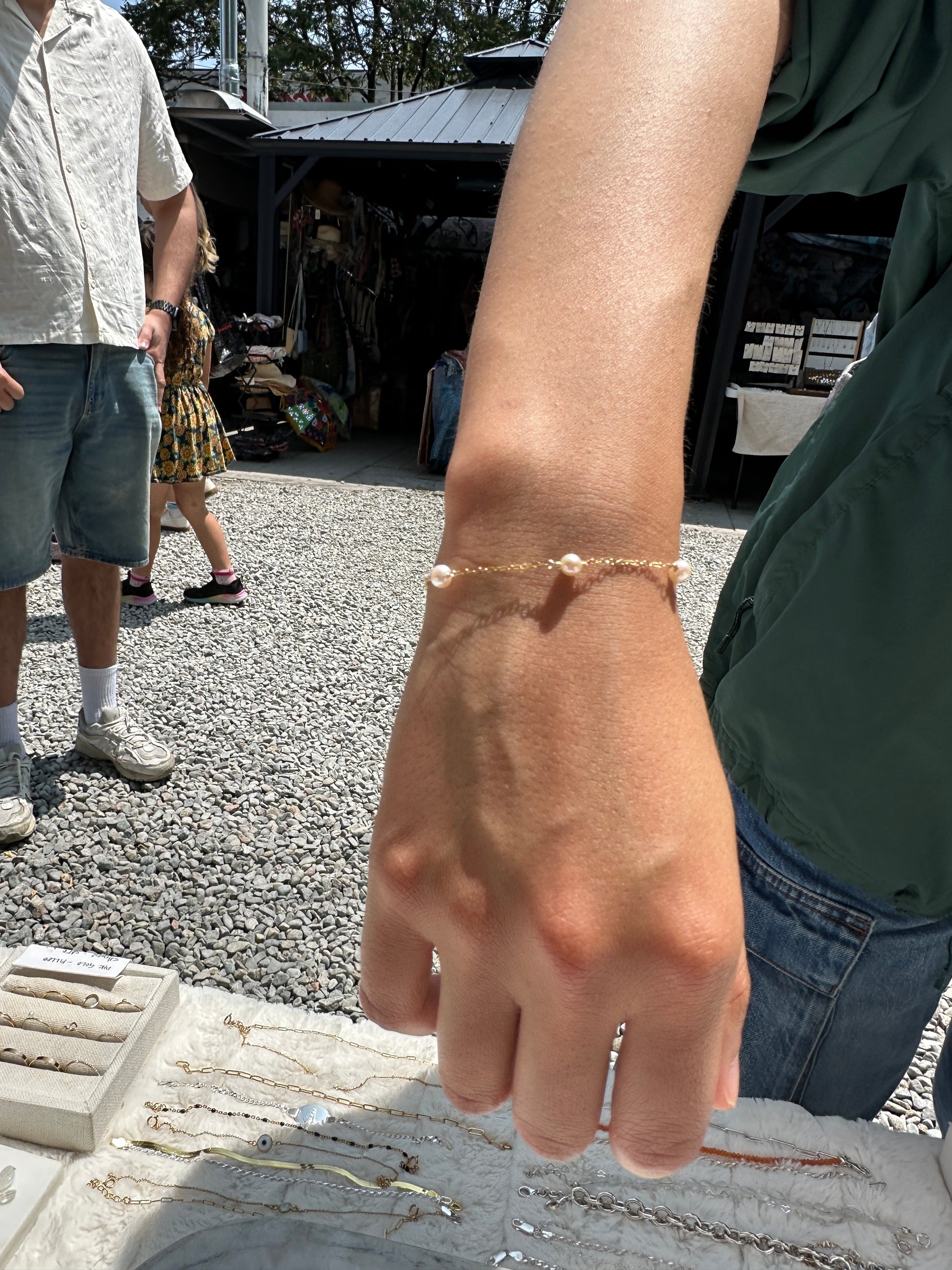 Close-up of a person's arm with a bracelet, with a blurred background of people and a building.