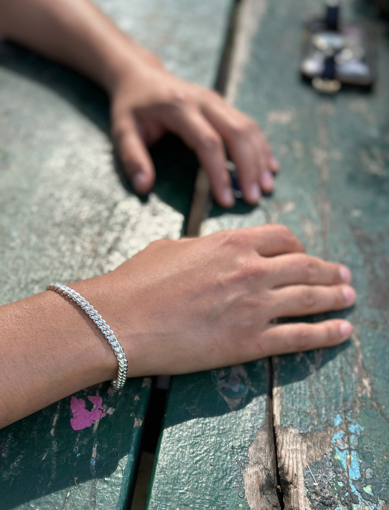 Close-up of a hand wearing a silver bracelet on a textured surface.
