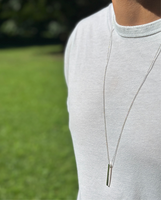 Person wearing a silver necklace with a blurred green outdoor background