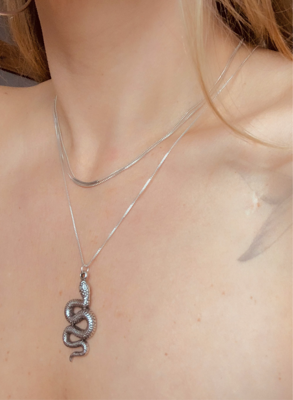Model is wearing layered necklaces in sterling silverl including a snake pendant