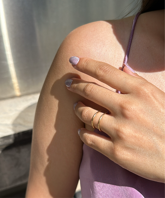 A person's hand wearing a gold-filled parallel ring, showing the ring's minimalist design and the person's nail polish.