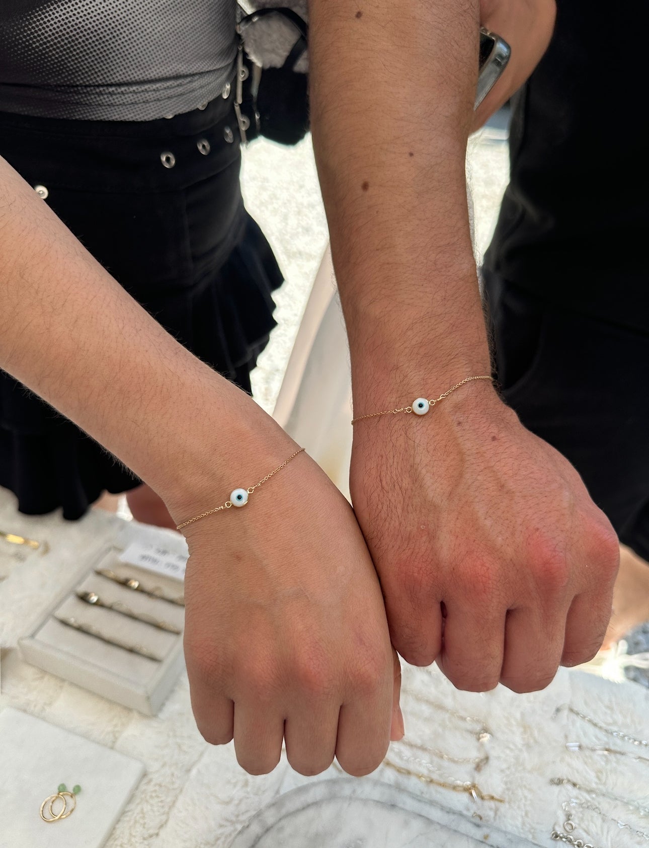 Two wrists wearing gold bff evil eye bracelets.