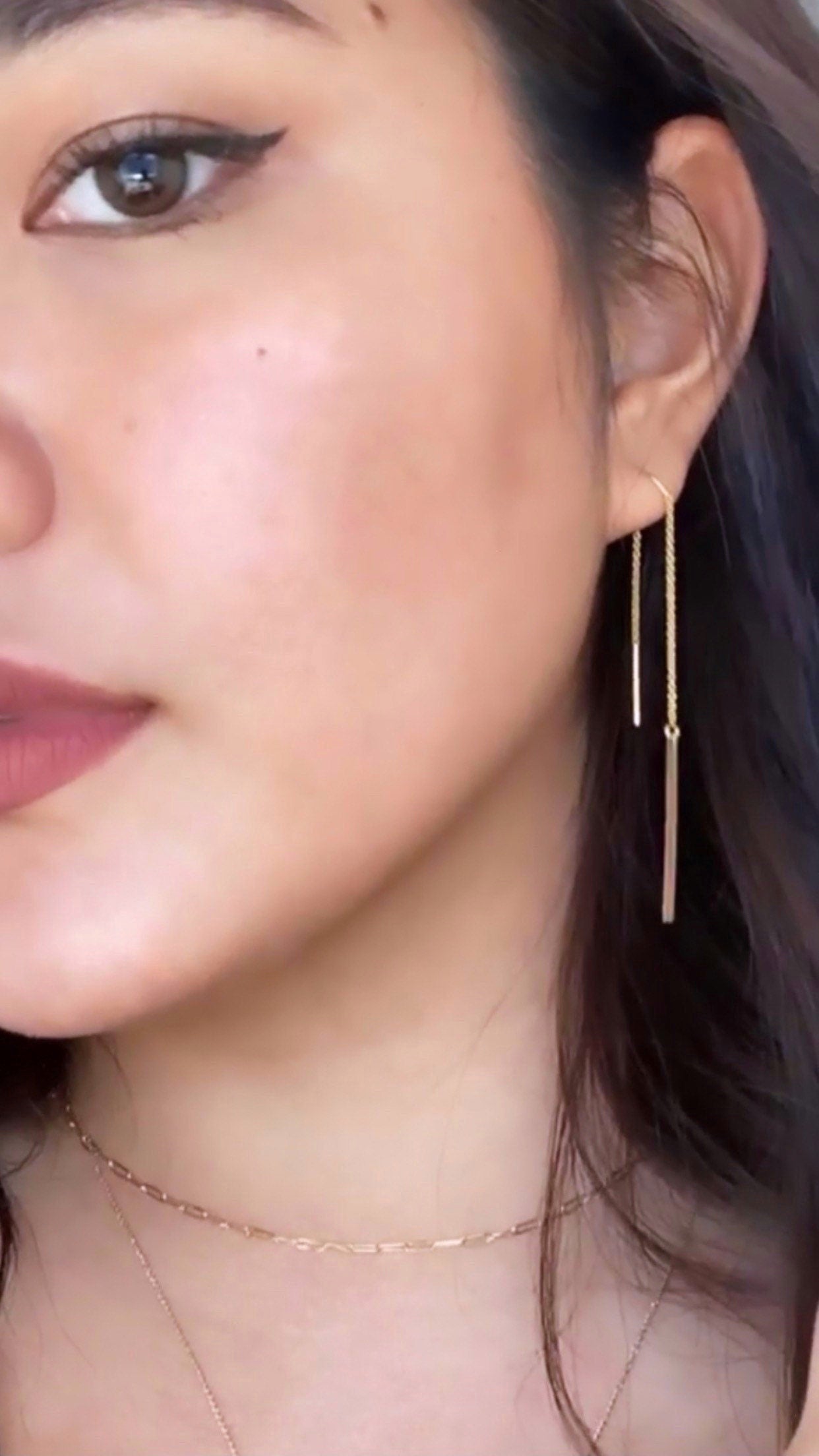 A person wearing minimalist gold-filled U threader earrings.