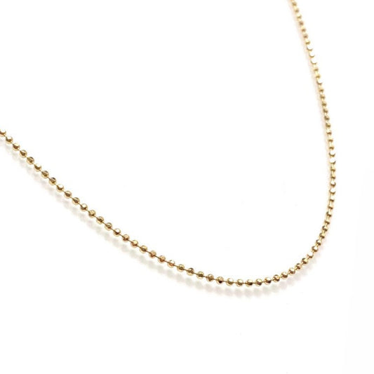 A gold ball chain necklace with faceted beads, laid out on a plain surface.