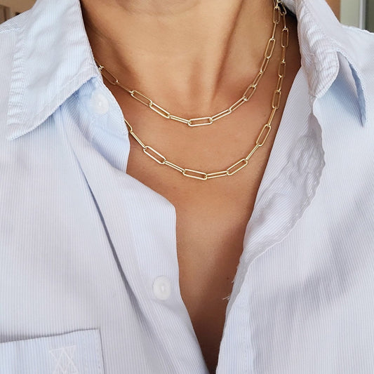 A person wearing a gold-plated sterling silver chunky paperclip chain necklace layered over a light blue shirt.