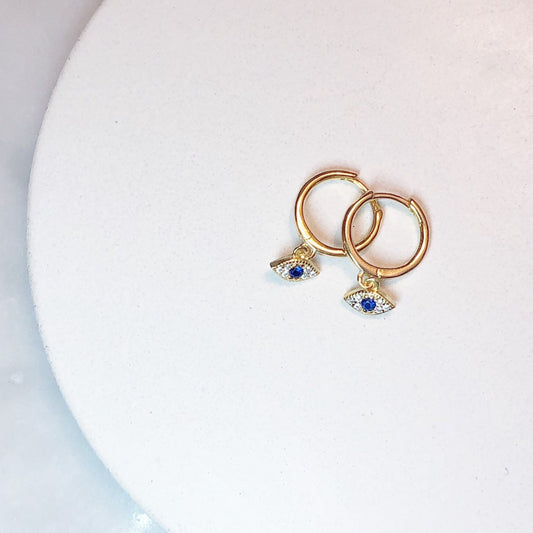A pair of gold-plated or sterling silver huggie earrings with white and blue cubic zirconia stones, displayed on a white surface.
