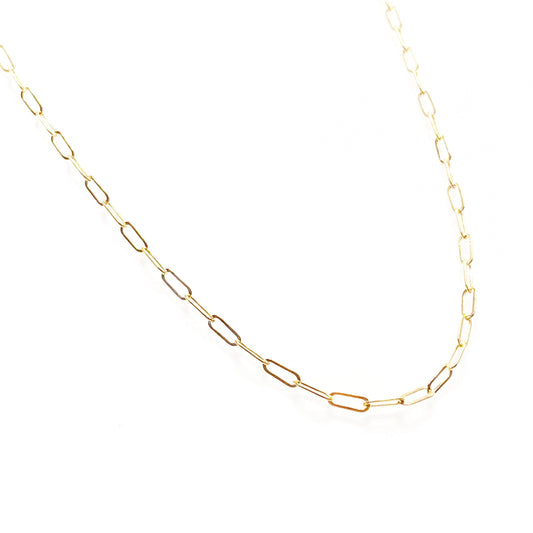 A gold-filled fine staple chain necklace laid out on a plain surface.