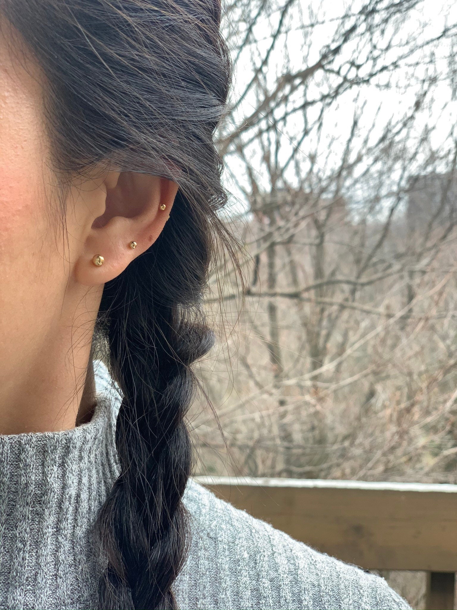 A person with a braided hairstyle wearing gold-filled ball stud earrings in different sizes.