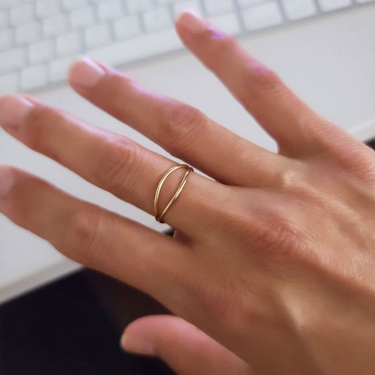 A gold-filled ring is worn on a person's finger, displaying a minimalist design with a unique wavy appearance.