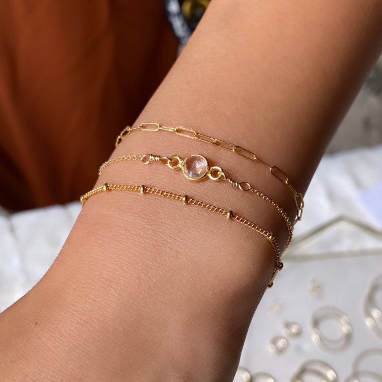A gold-filled or sterling silver satellite chain bracelet on a person's wrist, displayed alongside other bracelets.