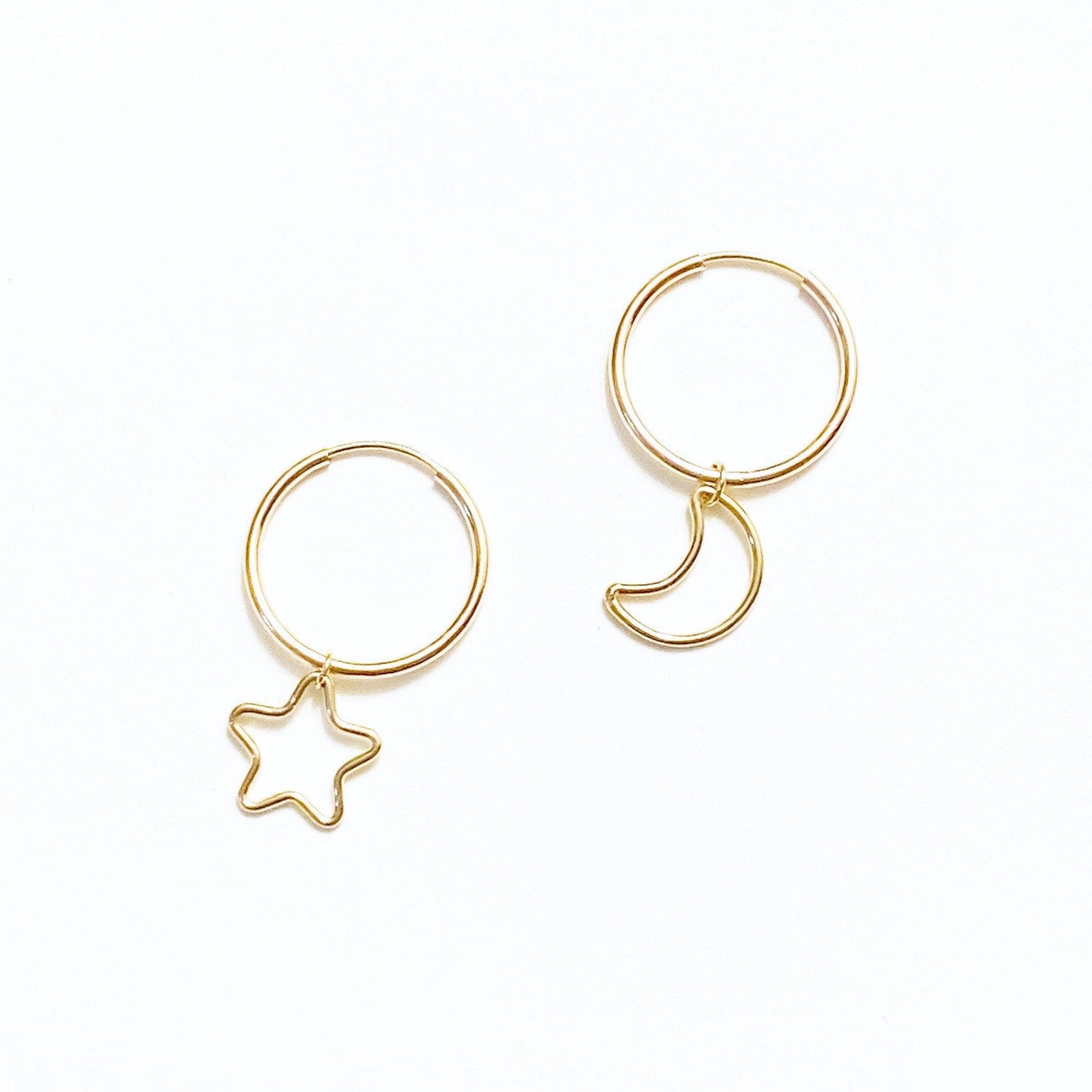 A pair of gold-filled hoop earrings, one with a dangling star charm and the other with a dangling moon charm.