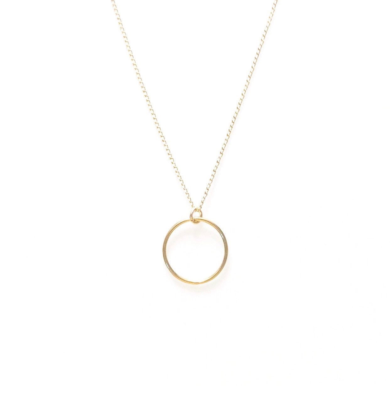A minimalist gold-colored necklace featuring a perfect circle pendant, displayed on a white background.