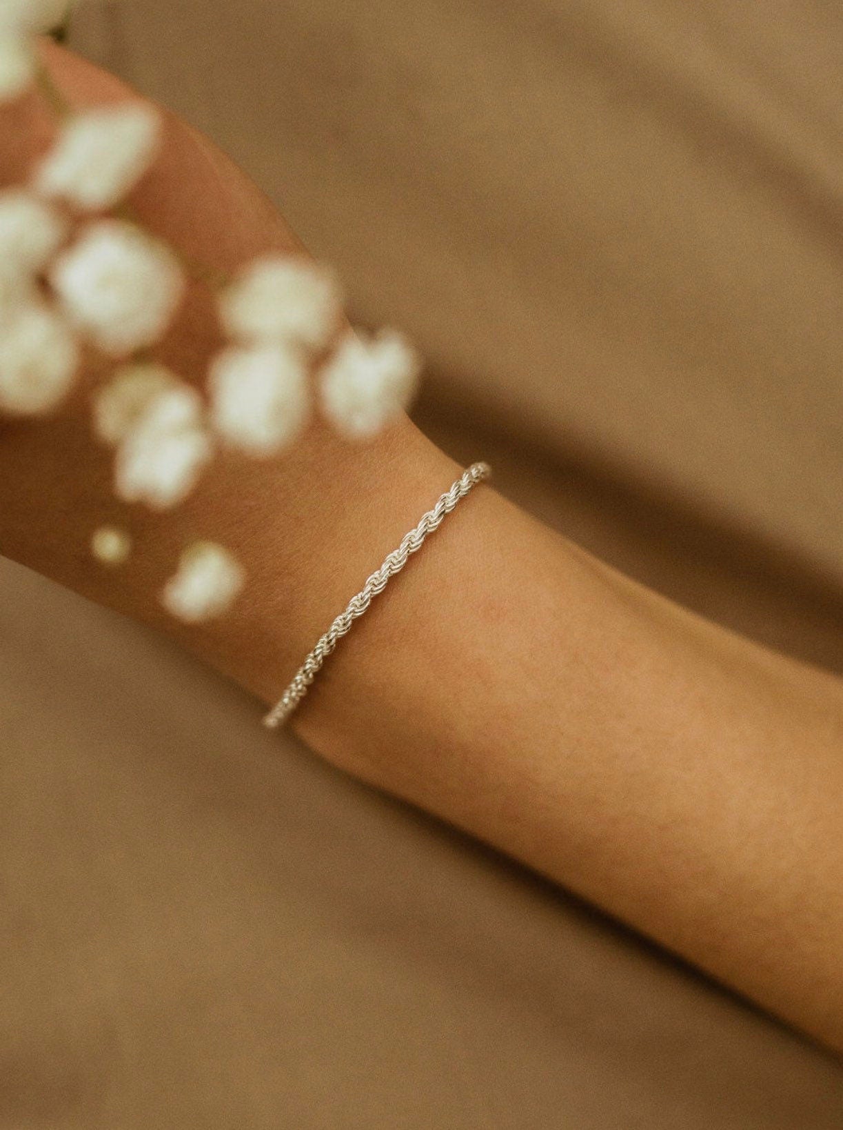 A sterling silver rope chain bracelet on a person's wrist, with a subtle sparkle visible in the light.