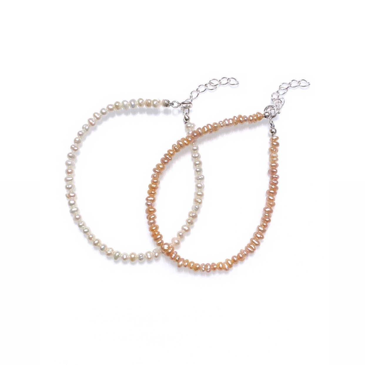 Two bracelets made of freshwater pearls, one in white and one in peach color, with sterling silver components, displayed against a white background.